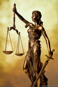 the scales of justice - a brassy statuette of a blindfolded lady justice with a sword and a set of balance scales, set against an artsy brown and yellow background